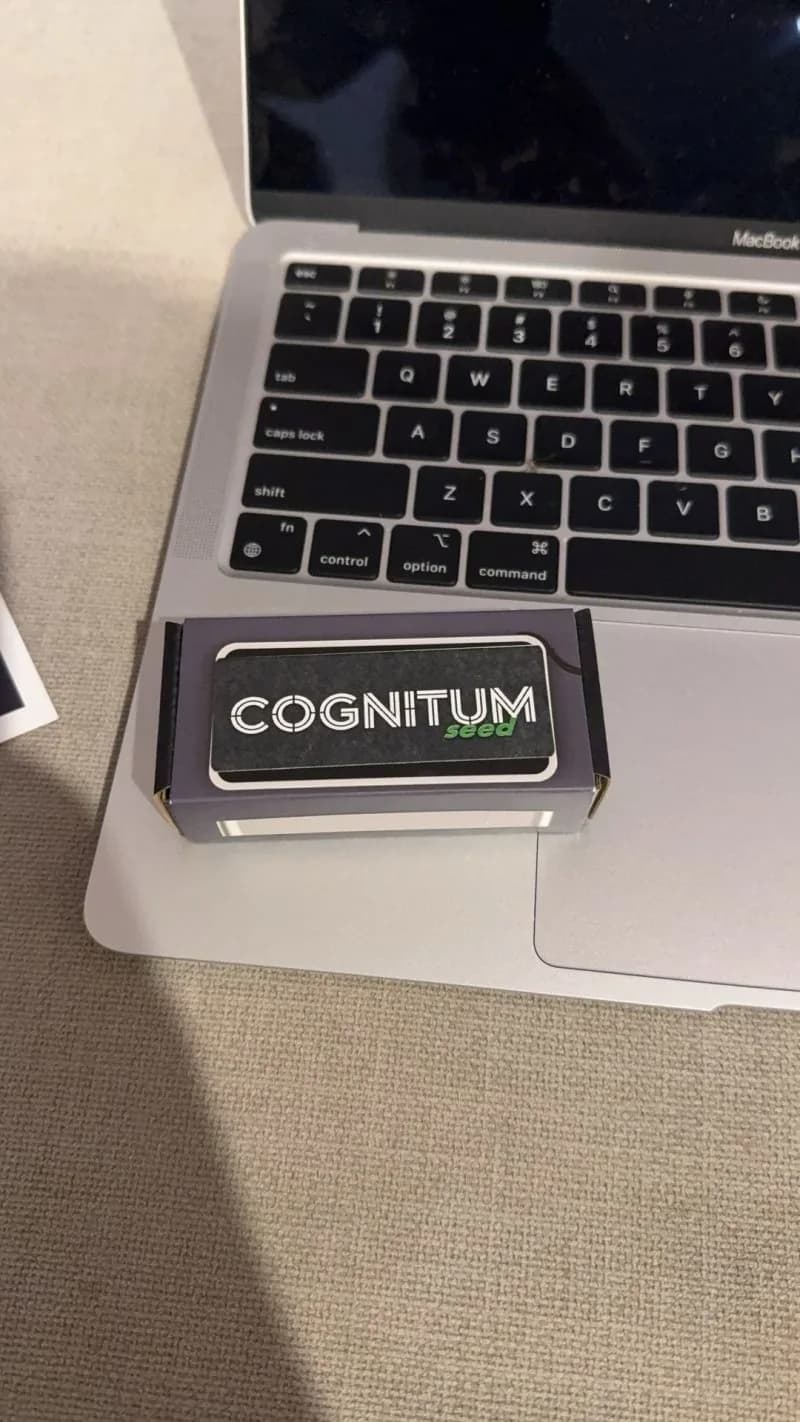 The Cognitum One Seed — a flat matte-black appliance with the COGNITUM wordmark on top, sitting on a MacBook keyboard for scale.